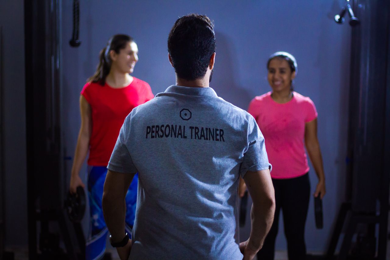 Crafting Captivating Headlines: Your awesome post title goes here Back view of a personal trainer guiding two women during a gym session indoors.